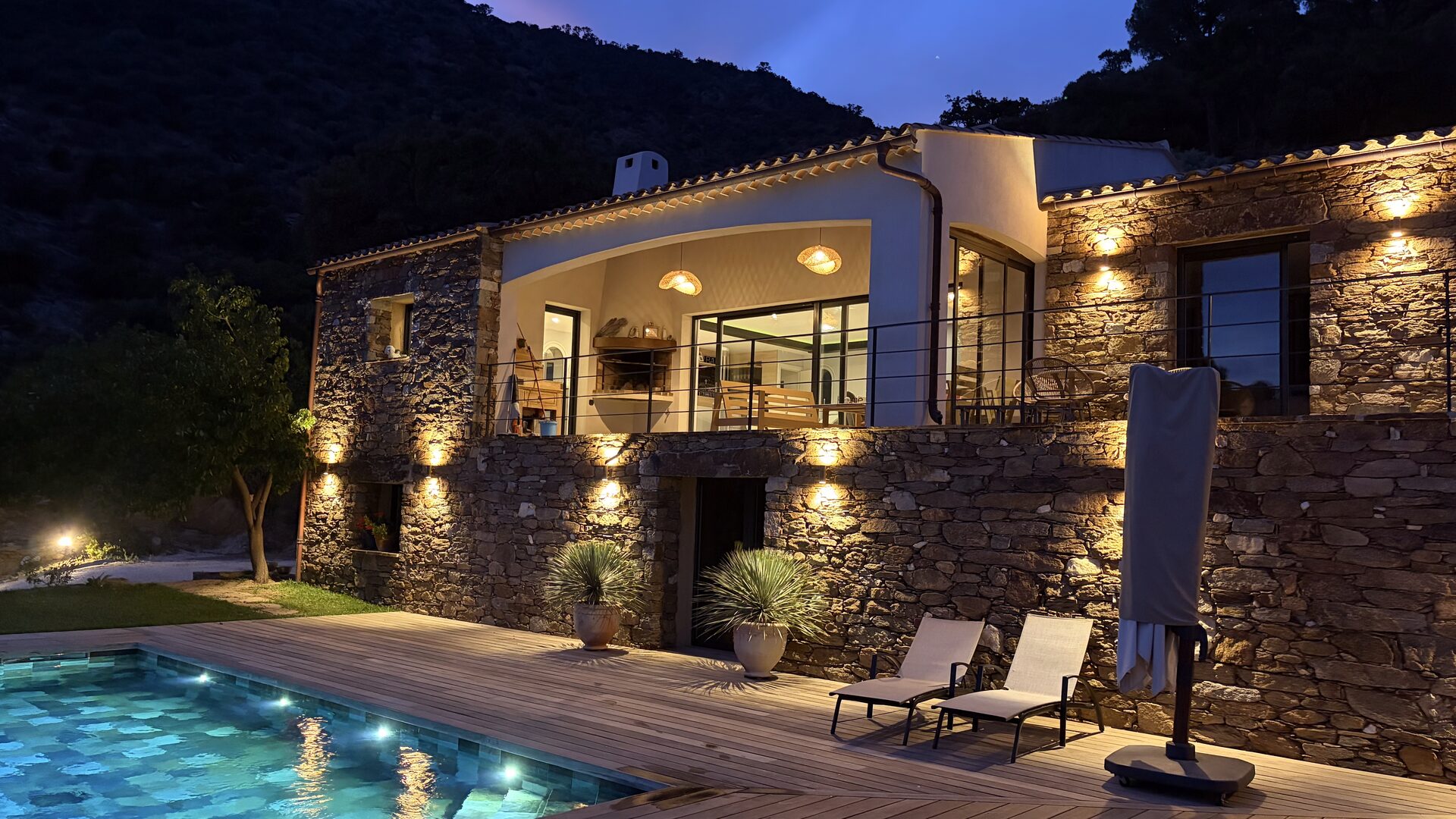 Villa en pierre mise en lumière à la tombée de la nuit : éclairage extérieur, terrasse et piscine